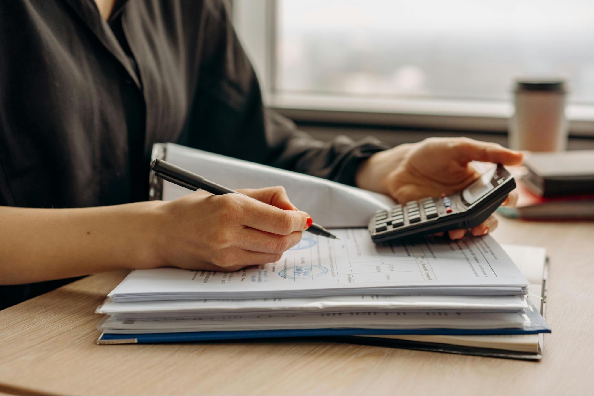 Two business professionals reviewing financial documents closely, using a magnifying glass and calculator to identify cost discrepancies in invoices.