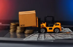 Miniature forklift lifting a shipping box beside stacks of coins, representing freight cost optimization, transportation savings, and cost reduction services.