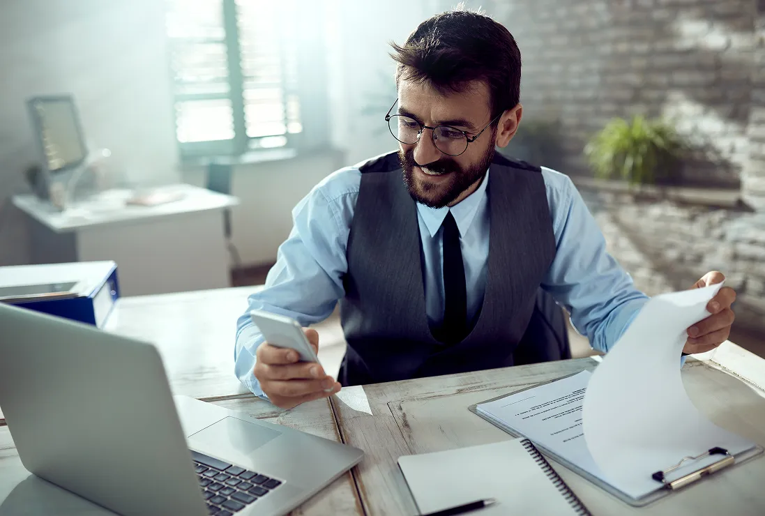 young-happy-businessman-going-through-reports-using-smart-phone-office 1 (1)