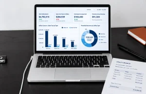 A laptop showing utility spending, sales tax paid, and estimated recovery alongside a utility invoice for sales tax recovery analysis.